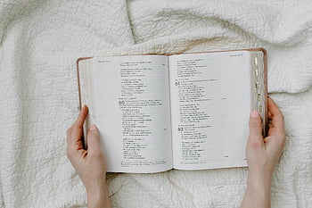 person holding book, open Bible, hands on quilt, religious themes, white quilted fabric, open book, reading Bible, spiritual reading, religious imagery, book photography, religious book