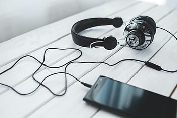 black vintage headphones, mobile smartphone, light wooden desk, portable music, technology, headphones and smartphone, desk setup, audio equipment, modern technology, music listening, tech accessories