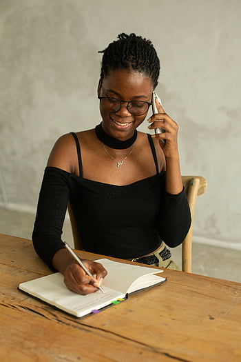 Černá žena, usmívající se žena, Psaní poznámky, telefonát, Vnitřní nastavení, Mladá žena, notebook, konverzace, brýle, dřevěný stůl, ležérní oblečení
