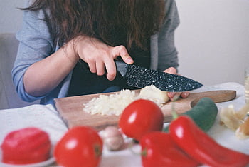 person cutting vegetables, chopping board, woman dicing onions, tomatoes, wooden cutting board, kitchen setting, close-up, food preparation, healthy eating, cooking, vegetables