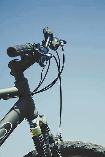 black bicycle, yellow handle bar, mountain bike, handlebar, clear blue sky, outdoor adventure, close-up, bike components, cycling, adventure sports, nature backdrop