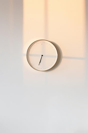round white analog clock, minimalist wall clock, elegant design, warm shadows, simple backdrop, analog timepiece, wall-mounted clock, modern decor, interior design, timekeeping device, minimalist style