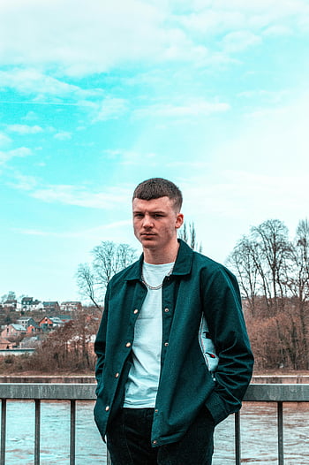 om care poartă sacou verde, tânăr, ținută la modă, stând pe pod, fundal pitoresc, stil urban, portret în aer liber, Fashion casual, aspect modern, vedere panoramică urbană, Tinuta eleganta