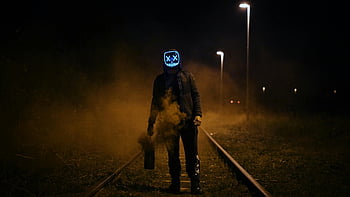 Neon -LED -Maske, Eisenbahngleise, Nachtszene, unheimliche Atmosphäre, neblige Umgebung, schwarze Jacke, stehende Figur, dunkle Einstellung, Fotografie im Freien, Stadterkundung, mysteriöse Atmosphäre