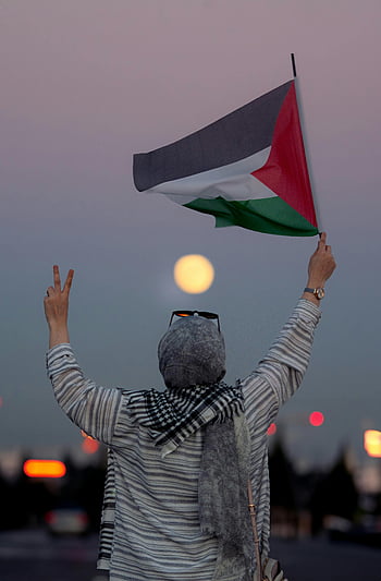 woman in headscarf, Palestinian flag, peace gesture, dusk, full moon, individual with headscarf, holding flag, evening scene, cultural symbol, protest gesture, peace sign