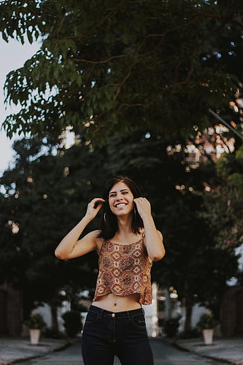 žena s úsměvem, dotýká vlasy, slunečný den, neformální móda, venkovní, veselý, Mladá žena, ulice, stromy, modní styl, Neformální outfit