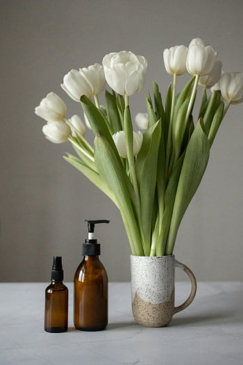 white tulips, ceramic vase, amber skincare bottles, bouquet, table, skincare products, floral arrangement, beauty products, still life, minimalist decor, white flowers