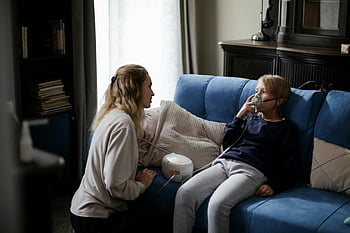 nemocný chlapec, modré dlouhé rukávy, sedí na gauči, Matka pomáhá, nebulizer, domácí péče, utěšit, péče o děti, nemocné dítě, Léčba rozprašovače, domácí ošetření