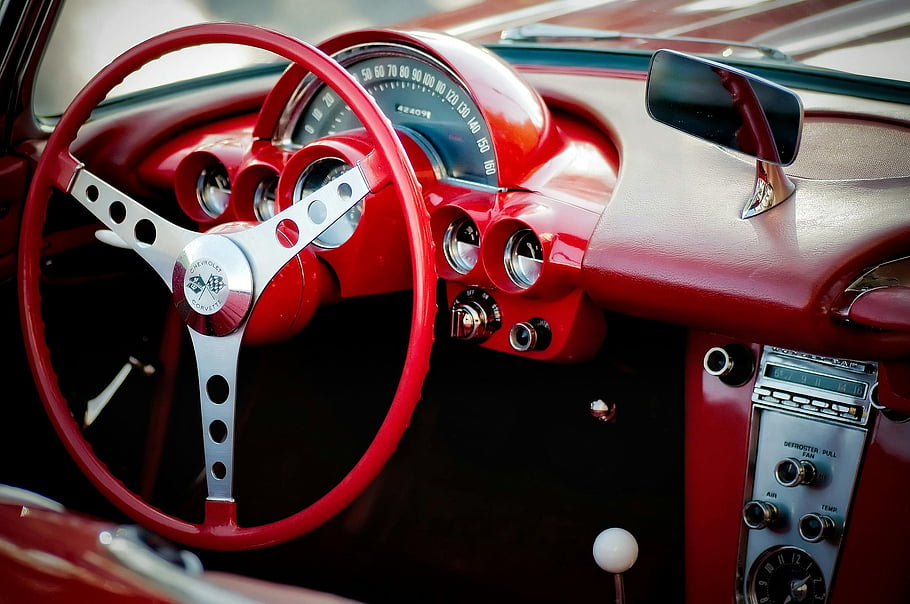 vintage Chevrolet Corvette, red interior, classic steering wheel, dashboard design, vintage car interior, red and gray vehicle, classic car dashboard, vintage Corvette, car interior design, classic car steering wheel, vintage car interior details