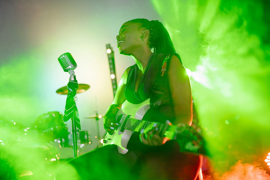 woman playing guitar, singing, live music performance, female guitarist, vocalist, vibrant green lighting, dynamic performance, stage performance, microphone, electric guitar, concert atmosphere