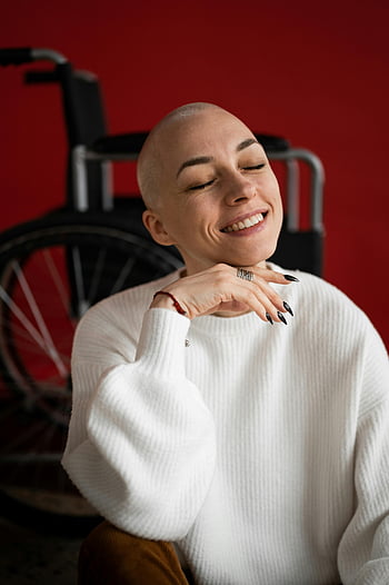 cheerful woman, smiling, wheelchair, recovery, bald woman, white sweater, red background, disability, hope, resilience, happiness