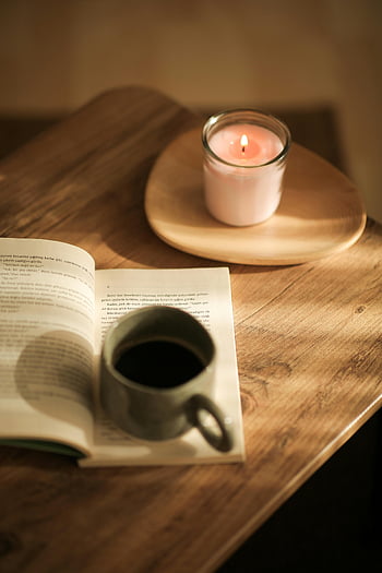 coffee mug, open book, lit candle, wooden table, warm scene, cozy atmosphere, reading time, coffee and books, candlelight ambiance, relaxing moment, home comfort