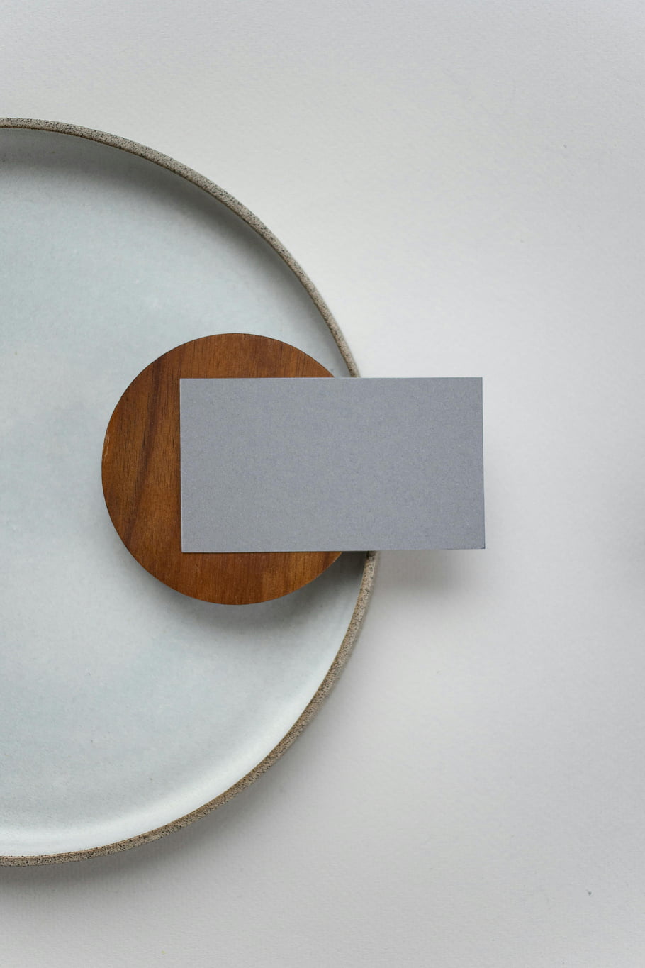 blank name tag, gray card, round wooden plate, modern table decor, flat lay, minimalist design, simple table setting, white background, clean aesthetic, modern decor, wooden coaster