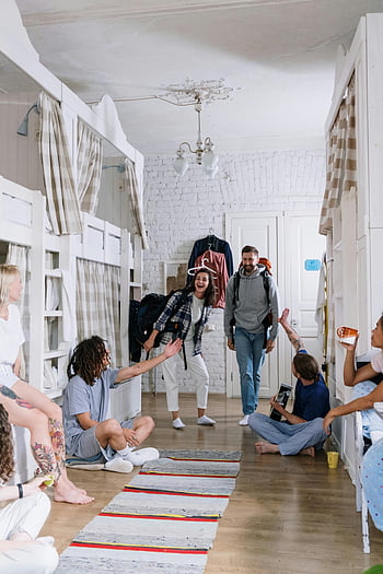 friends gathered, diverse backpackers, cheerful socializing, cozy dorm room, lively atmosphere, group interaction, backpackers meeting, dorm room gathering, friends in dorm, social atmosphere, diverse group