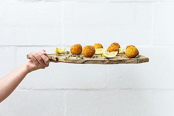 Bile de Arancini, felii de lamaie, bord de lemn rustic, Masă proaspătă, masă sănătoasă, persoană care ține, Tocător, Arancini gustoși, felii de lămâi, Consiliul de servire din lemn, mancare sanatoasa