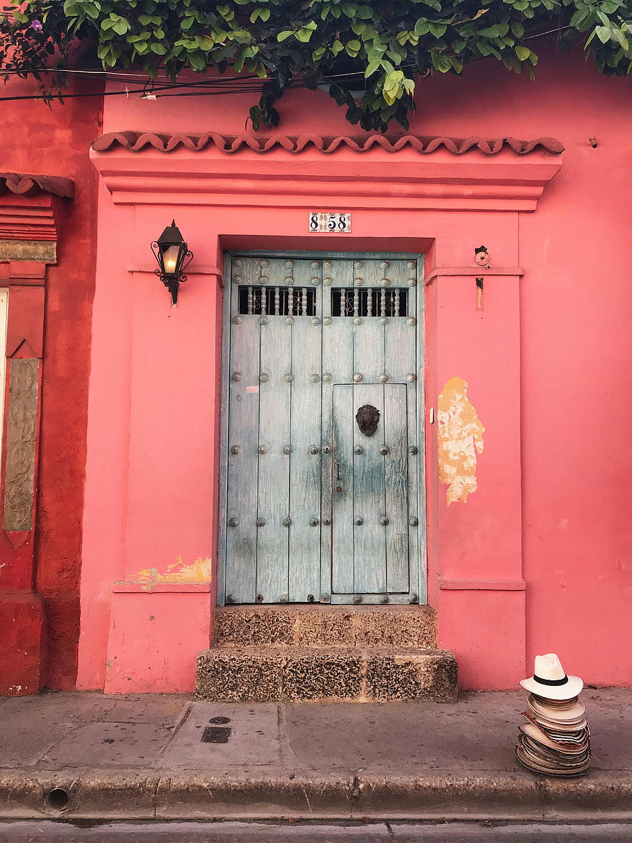 pink wall, double door, vintage wooden door, vibrant pink walls, Cartagena, travel inspiration, house entrance, colorful architecture, colonial style, street scene, hats and books