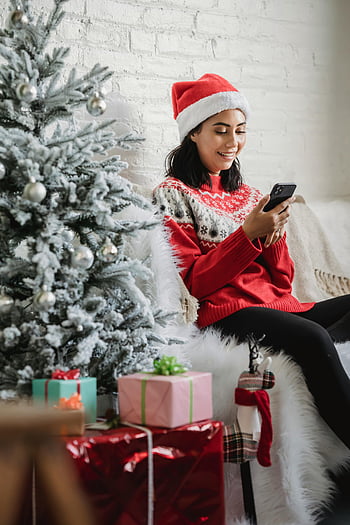 santa-hattu, iloinen nainen, älypuhelin, joulukuusi, koristeltu puu, lahjat, juhlava, lomakausi, talvi-, kodikas, hymyilevä