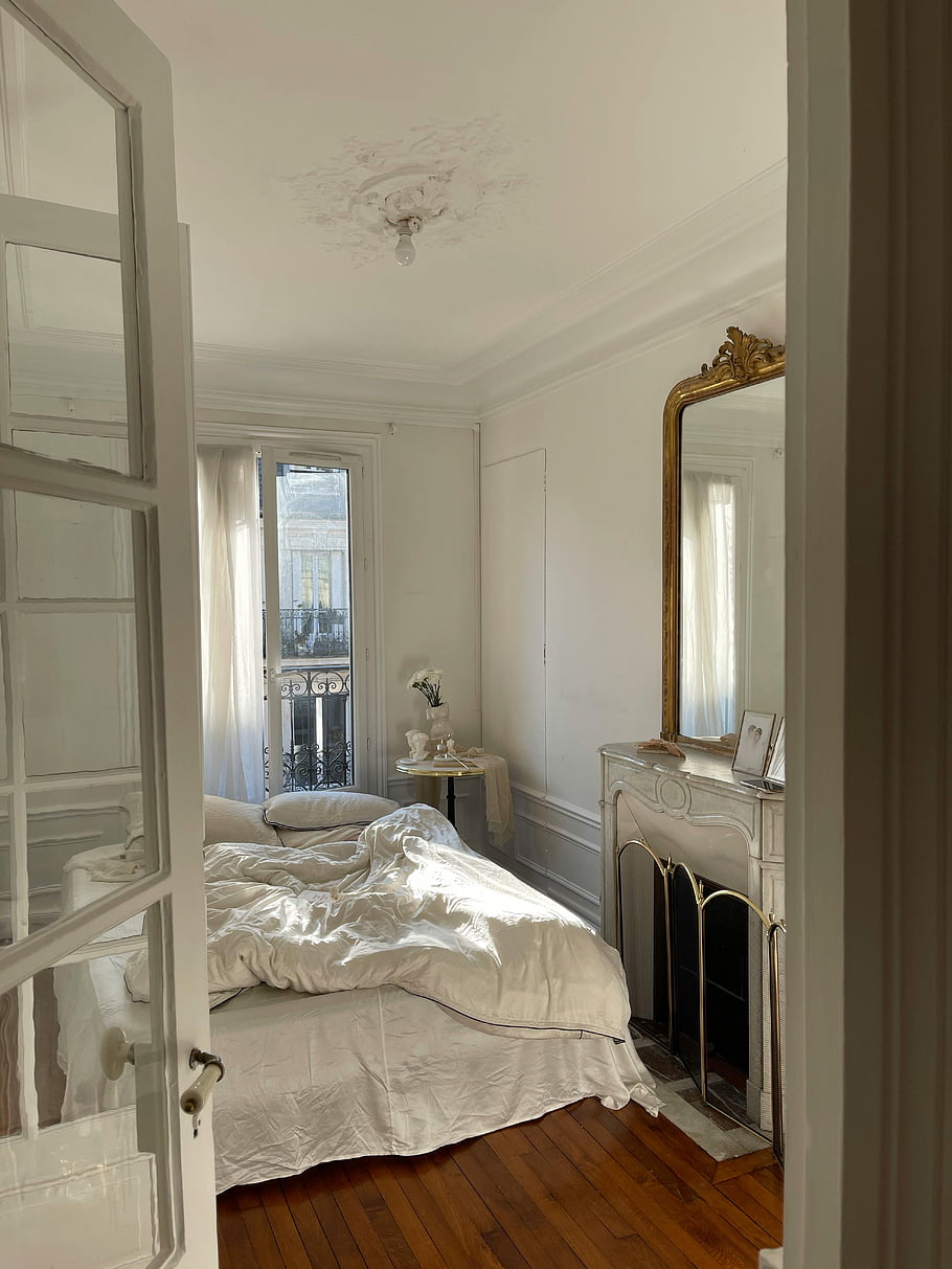 modern French style bedroom, elegant French-style bedroom, vintage decor, natural light, white bedroom, ornate mirror, wooden floor, French interior, classic bedroom, cozy bedroom, French decor