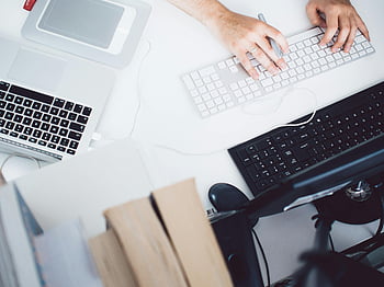 person typing, black keyboard, gray keyboard, office desk, computer setup, work environment, hands on keyboard, laptop, desktop monitor, workspace, office supplies