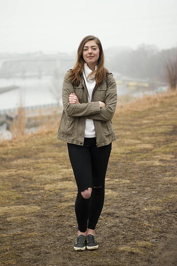 Žena v šedé bundě, černé tísňové kalhoty, překročení zbraní, mlhavý břeh řeky, ležérní oblečení, moderní móda, životní styl, Mladá žena, venkovní nastavení, Ležérní styl, bílý rolák