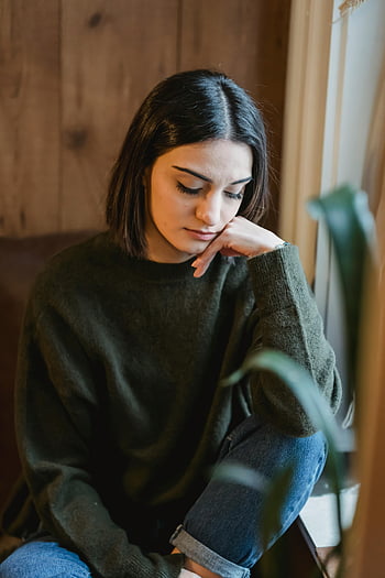 donna triste, abbigliamento casual, seduto vicino alla finestra, giovane donna, pensieroso, umore contemplativo, Accogliente impostazione interna, maglione verde, Blue jeans, Scena indoor, muro di legno