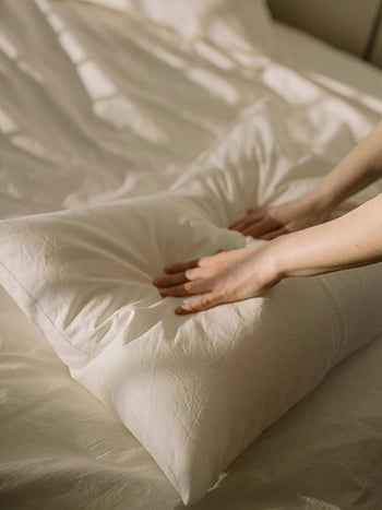 hands arranging pillow, white bed, neatly made bed, cozy atmosphere, close-up hands, white pillow, bed linens, soft bedding, bedroom decor, comfort, relaxation