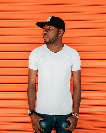 man, white crew-neck t-shirt, black cap, fashionable, young man, casual wear, confident pose, vibrant orange backdrop, street style, urban fashion, casual outfit