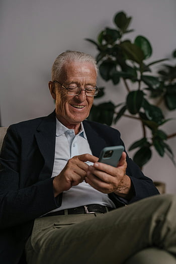 eldre mann, svart jakkesjakke, smarttelefon, smilende, komfortable omgivelser, innendørs, briller, uformell klær, Teknologibruk, pensjonist, moderne livsstil