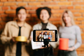 women promoting product, man promoting product, diverse team, vloggers recording, smartphone video, brick wall backdrop, product promotion, team vlogging, social media content, content creation, influencer marketing